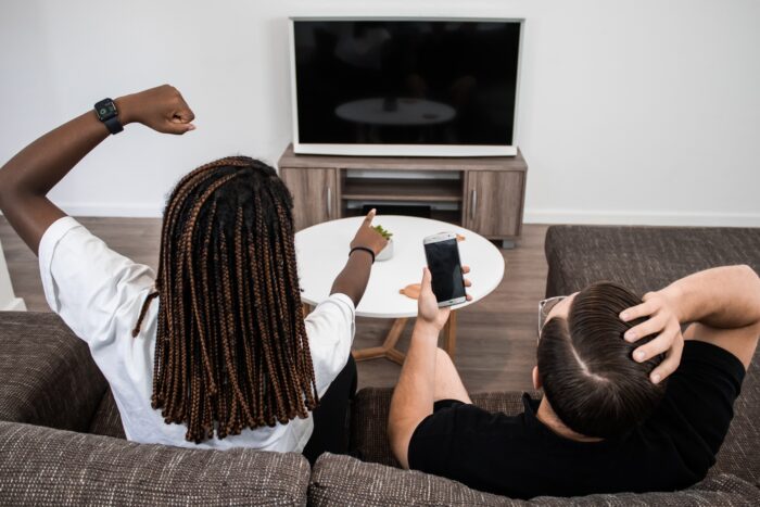 Gamification in Filmen - Zwei Menschen mit Smartphone sitzen auf dem Sofa vor dem Fernseher